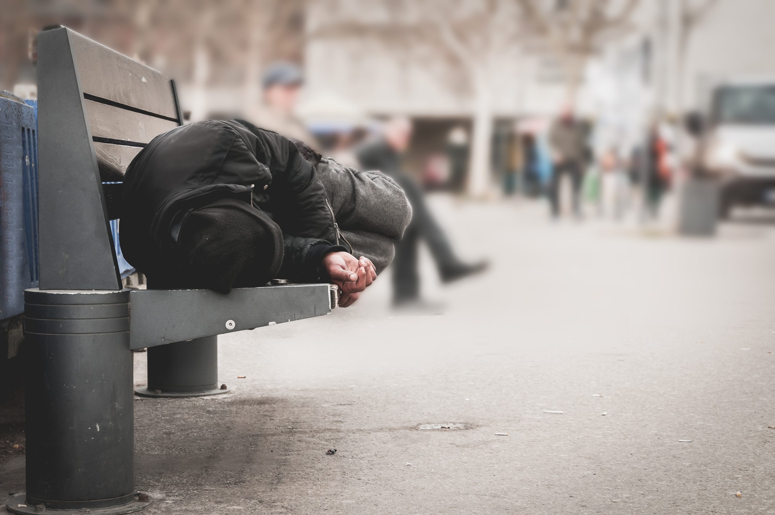photo of a person experiencing homelessness sleeping on a bench in a city, emphasizing the challenges faced by individuals with severe mental illness who lack stable housing