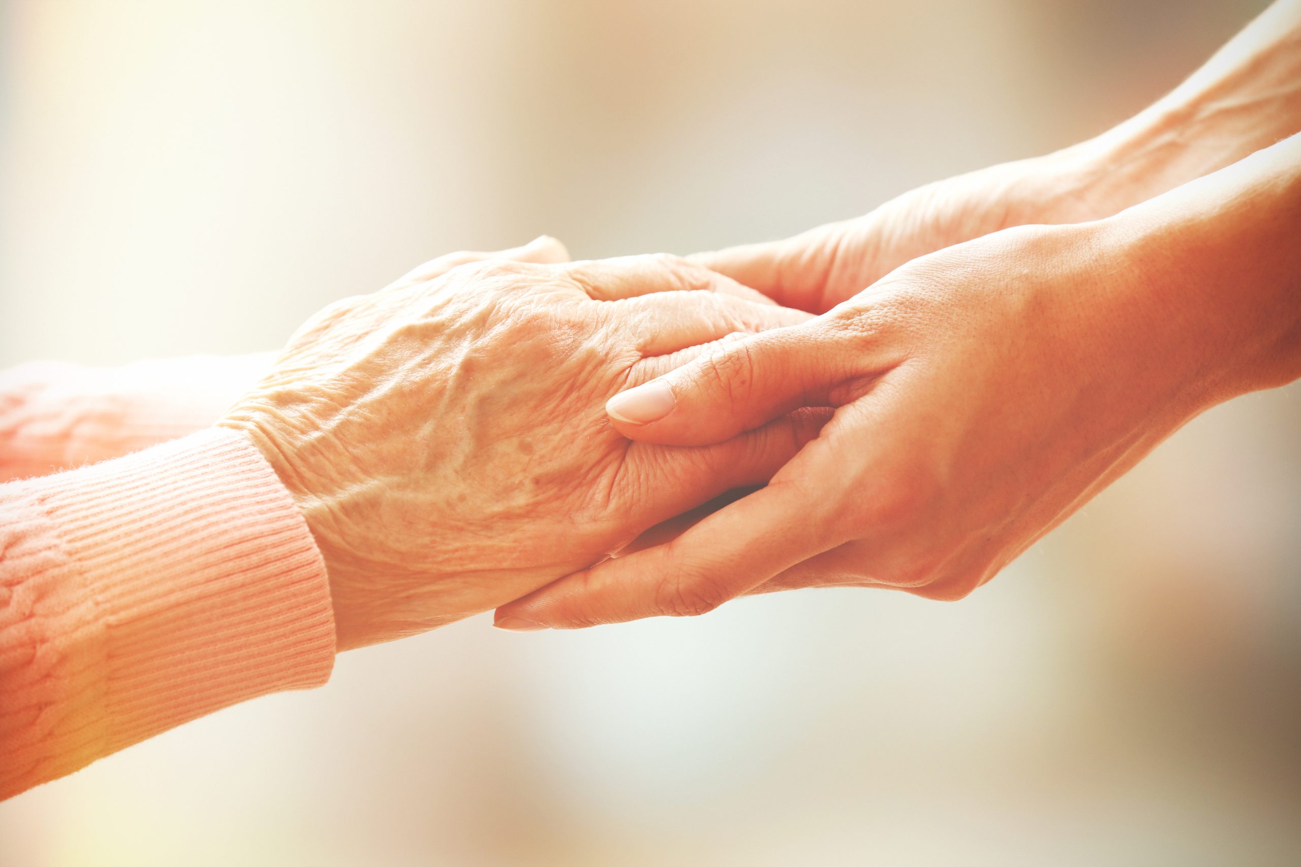 image of middle-aged hands gently holding a pair of elderly hands, symbolizing the care and support provided by families to aging loved ones with severe mental illness